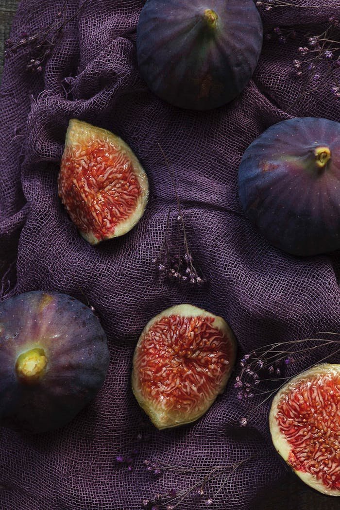 Aesthetic flat lay of fresh figs on a textured purple fabric background.