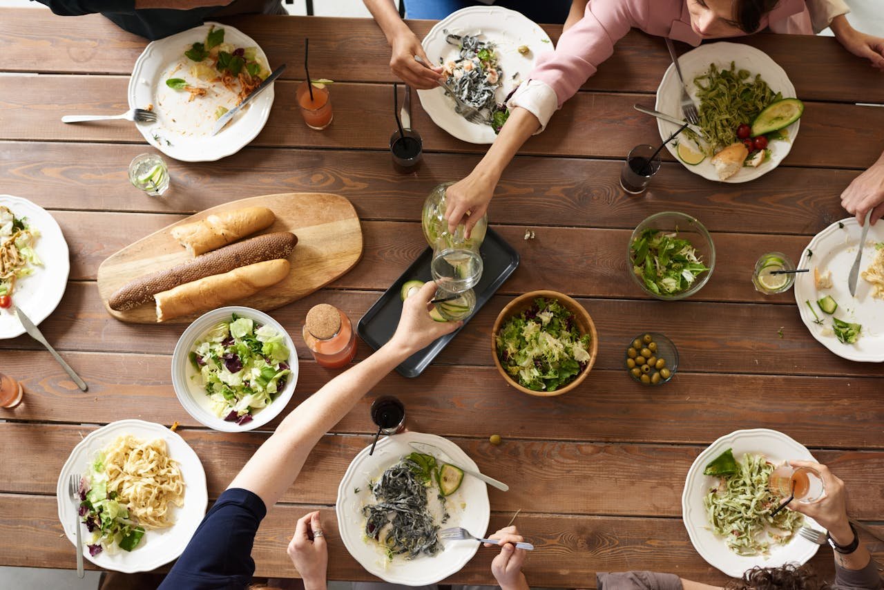 services-01 An overhead shot of a dining table featuring various pasta dishes and salads shared by a group.